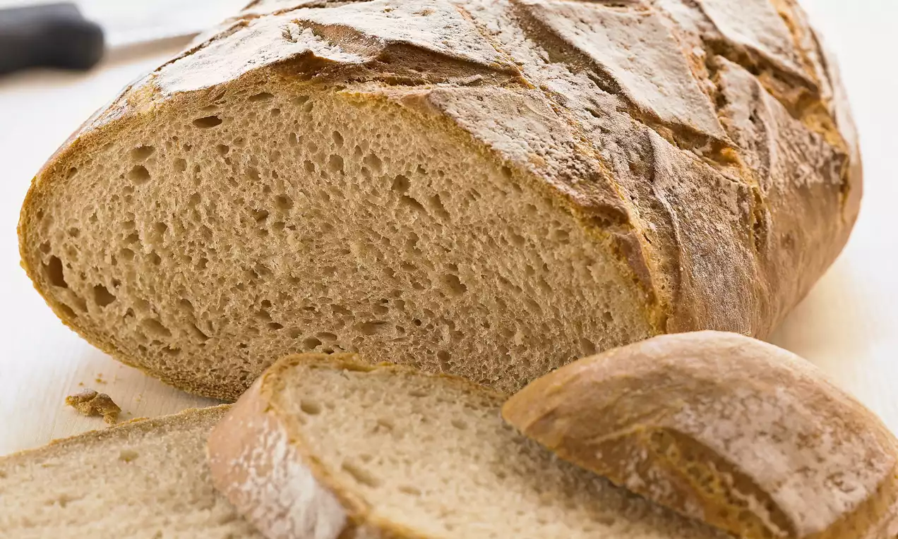 Pain brun à la croûte dorée et légèrement farinée, tranché pour révéler une mie dense et alvéolée sur une surface claire