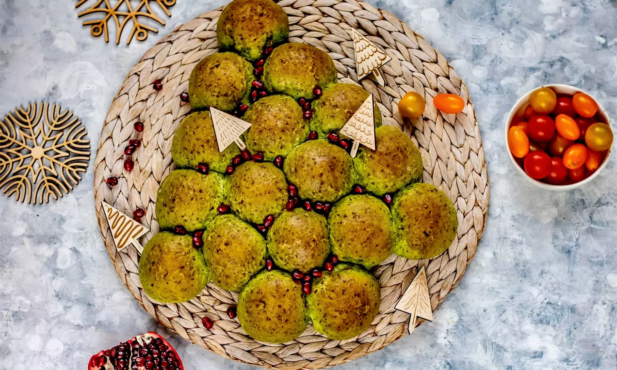 Постна питка с яркозелени кръгли питчици от спанак в триъгълна елховидна форма, декорирана с червени семена и дървени фигурки върху плетен поднос