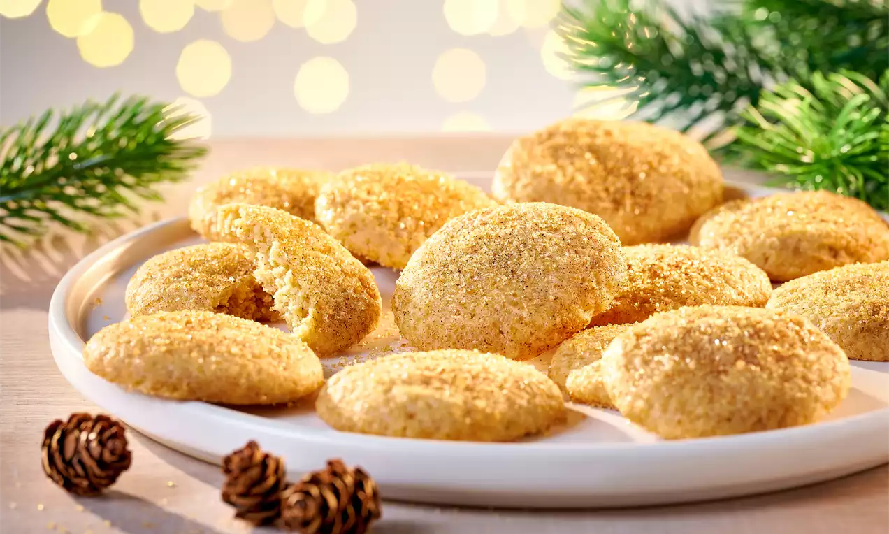 Goldbraune, runde Snickerdoodles mit knuspriger Zimt-Zucker-Kruste auf weißem Teller, dekoriert mit Tannenzweigen und kleinen Zapfen