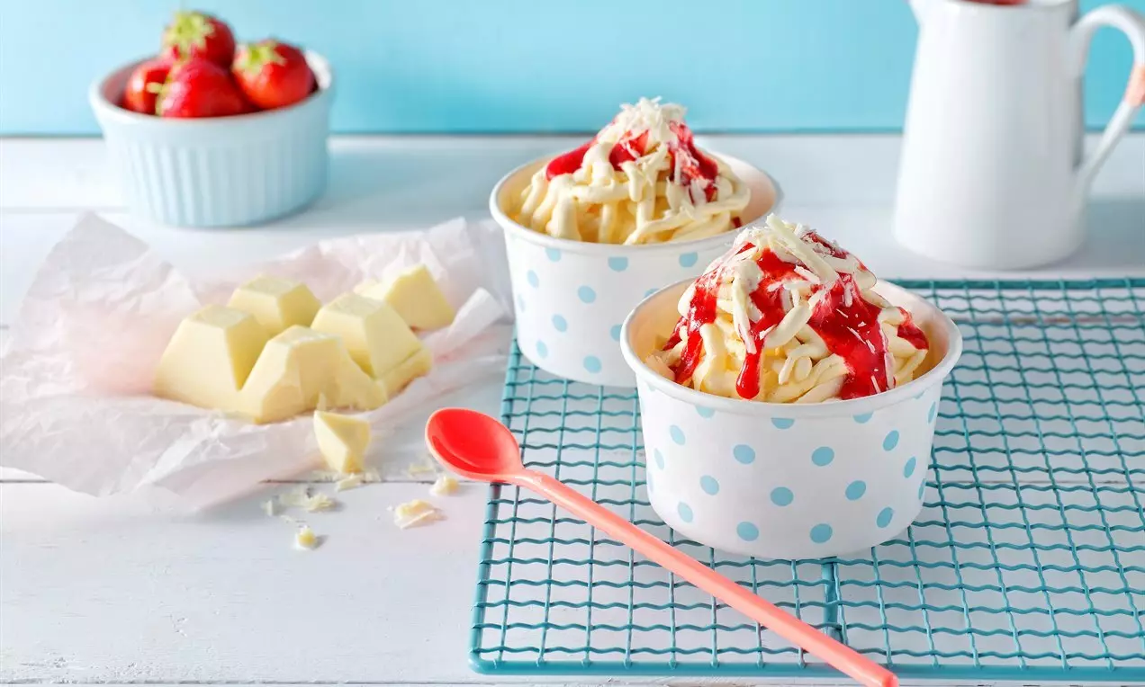 Кремообразен ванилов сладолед в бели чашки на сини точки, украсен с яркочервен сос и стърготини бял шоколад върху метална решетка