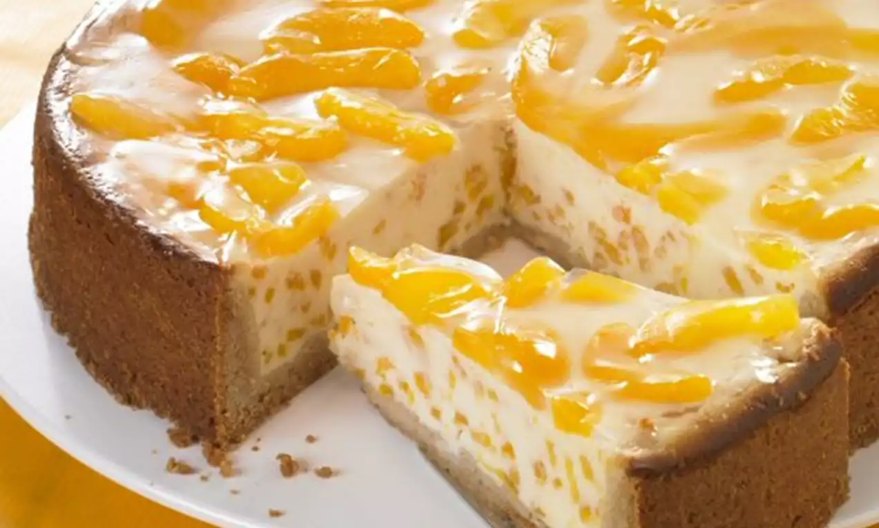 Aprikosen-Quark-Kuchen mit goldbraunem Rand, weißer cremiger Füllung und glänzenden Aprikosenspalten auf einem weißen Teller