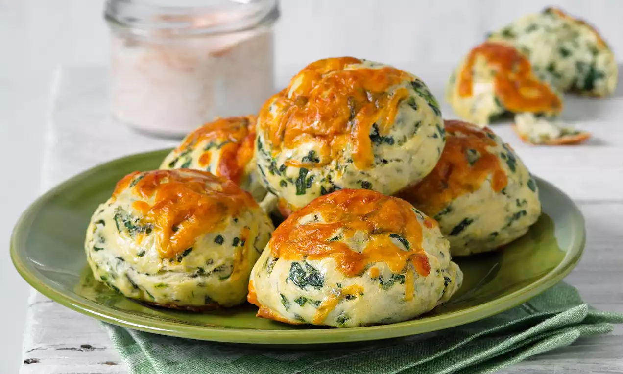 Špenátové koláčky zlatohnědé a jemně nadýchané, s tmavozelenými kousky špenátu, uspořádané na hladkém zeleném talíři s látkovým ubrouskem