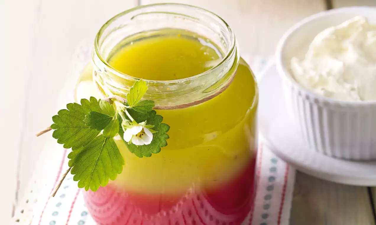 Staklenka s džemom u dvije boje, crvenom pri dnu i zelenožutom pri vrhu, ukrašena svježim listom i cvijetom ogrozda na poklopcu