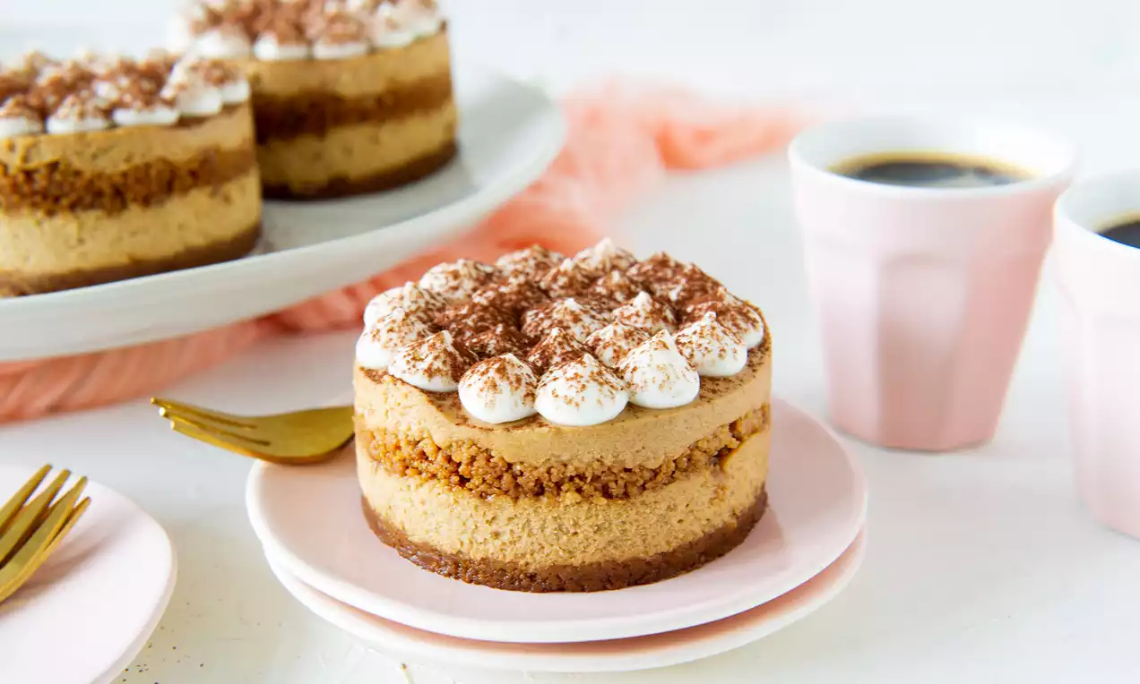 Ronde MonChou Tiramisu met laagjes beige room en bruine cake, afgetopt met witte slagroom en cacao op een roze bord naast koffie in pastelroze kopjes
