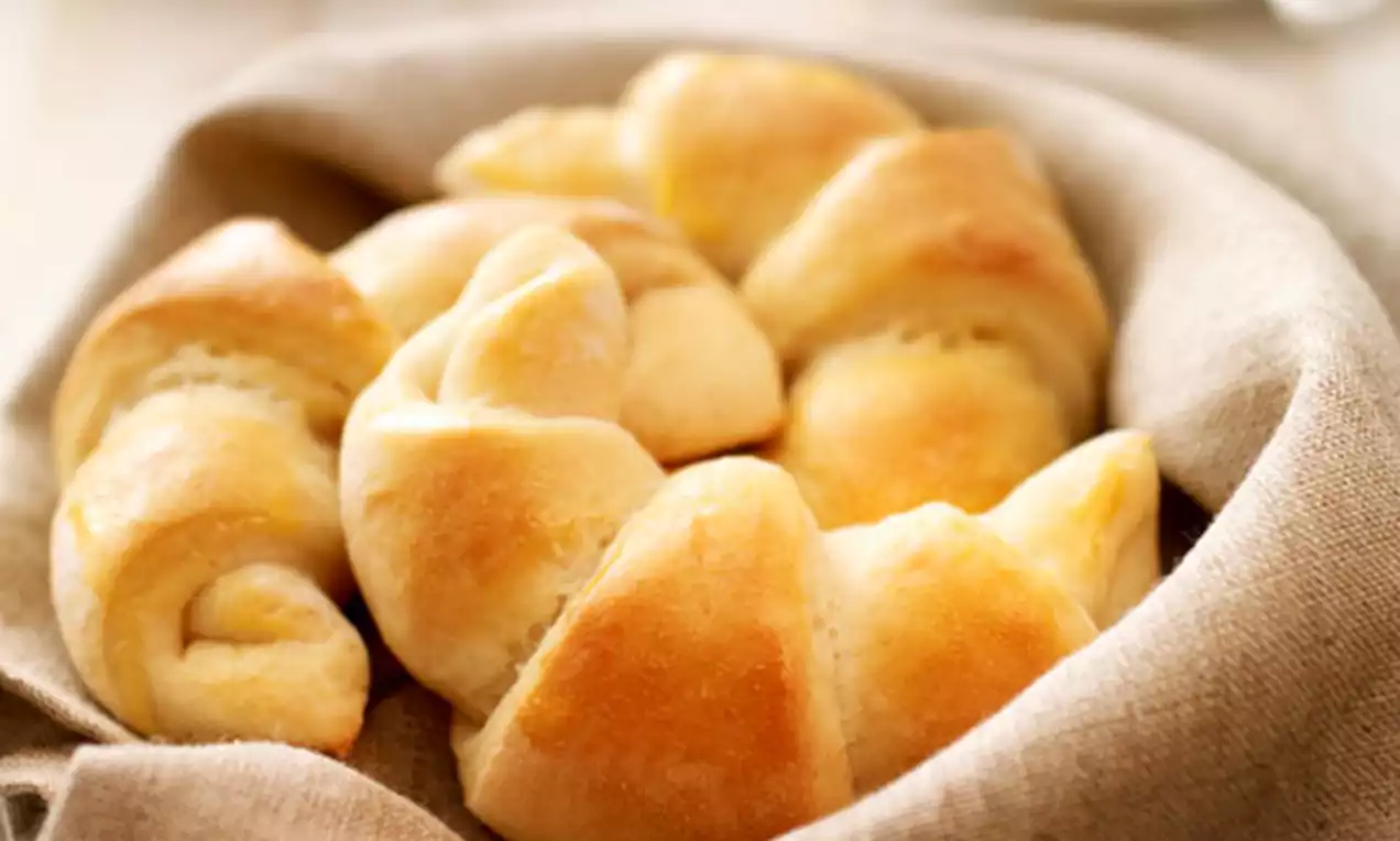 Croissants dorés au fromage blanc aux bords légèrement courbés, posés dans un linge beige plié sur une table en bois clair