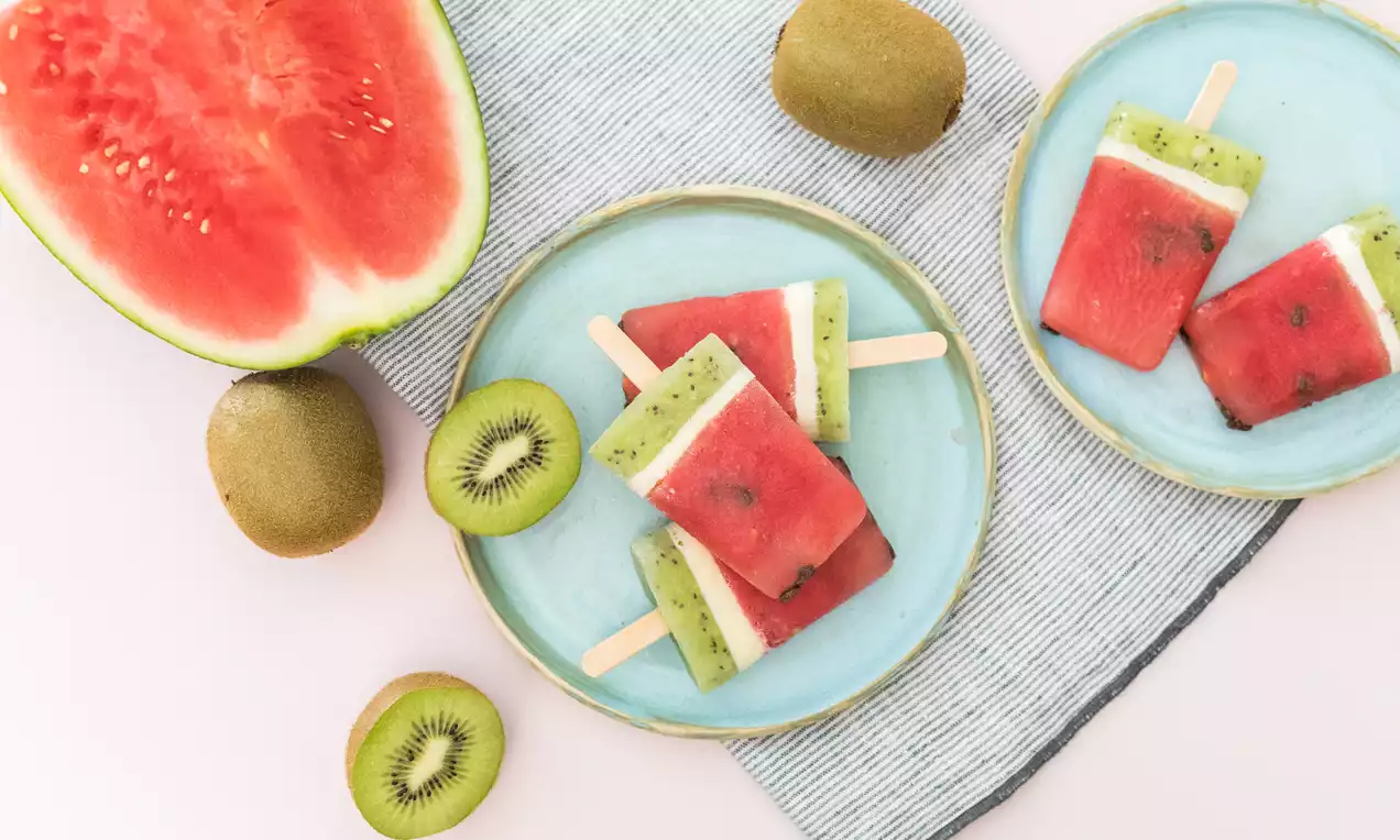 Polos rectangulares de sandía roja con capa de kiwi verde moteado y blanco, sobre platos azul claro con rodajas de kiwi y media sandía