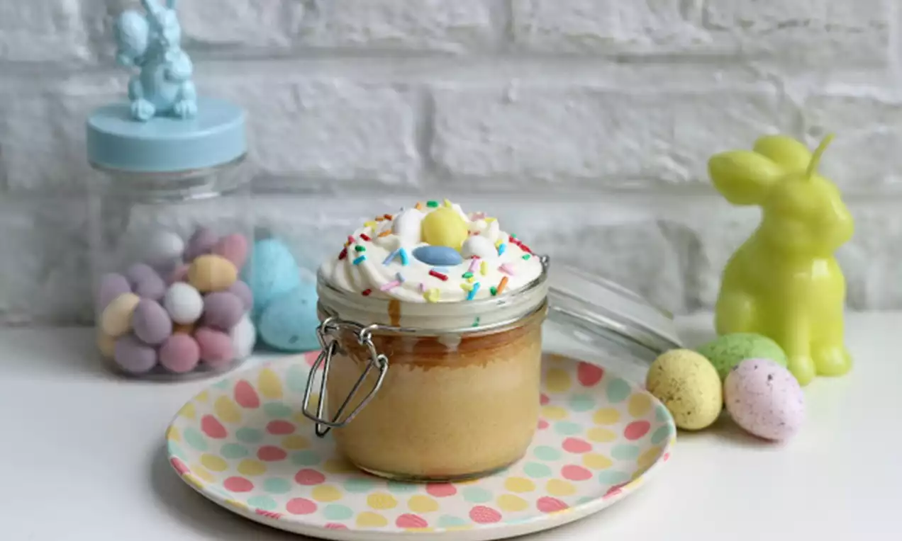 Cupcake in een glazen potje met glanzende witte slagroom, felgekleurde sprinkles en een pastel chocolade-eitje op een stippenbord