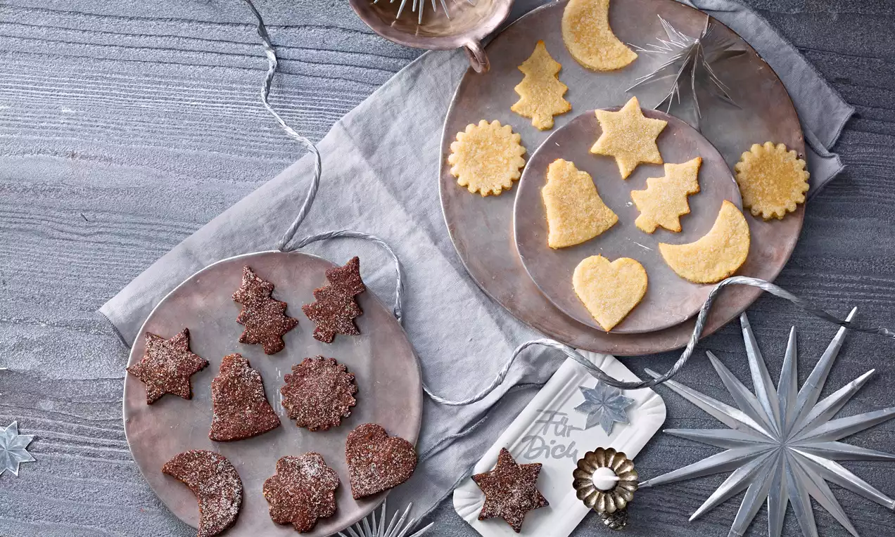 Schweizer Brunsli in dunklem Schokoladenbraun, stern- und tannenförmig, mit Zuckerkristallen bestäubt auf einem grauen Teller angerichtet