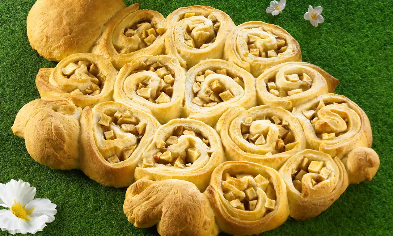 Goldbraunes Osterlamm aus luftigem Teig mit sichtbarer Apfelfüllung, in Form von Schnecken angeordnet, dekoriert auf grünem Untergrund