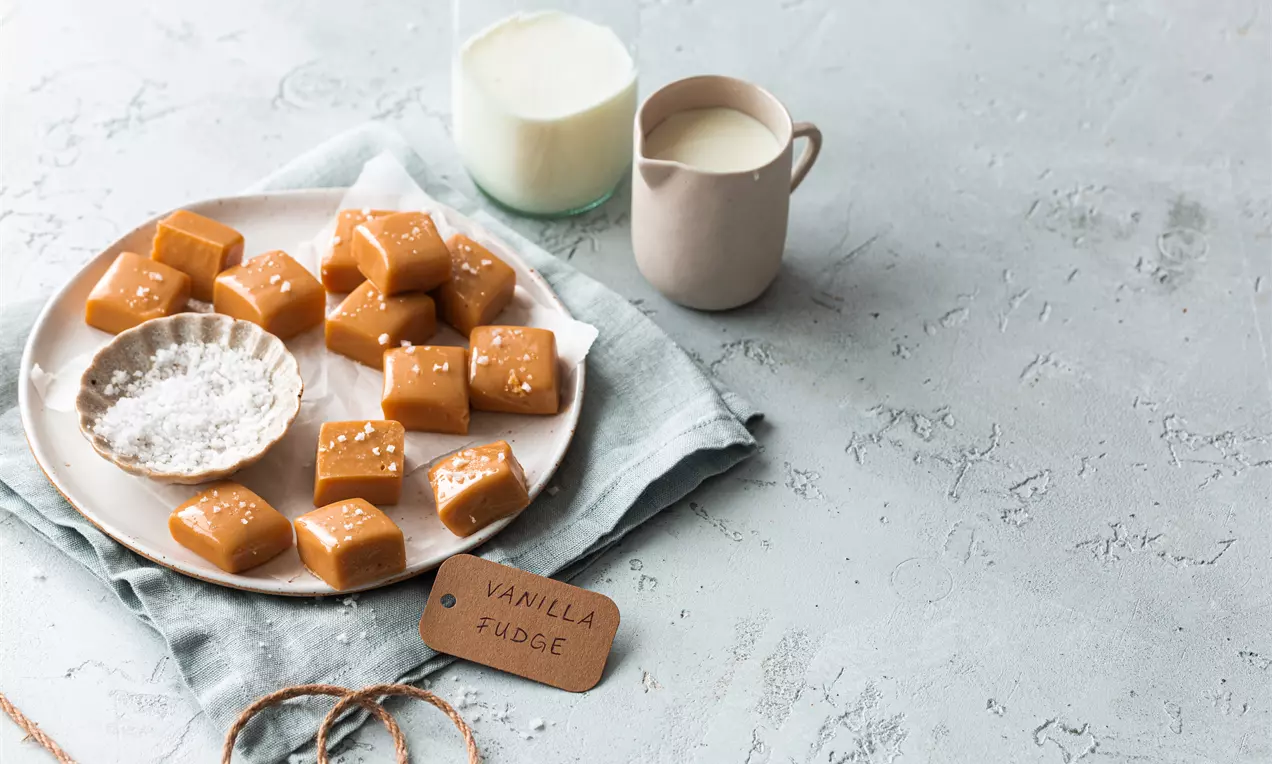 Picture - Carrés de fudge vanille couleur caramel clair parsemés de cristaux de sel sur une assiette blanche avec un pot de lait à côté