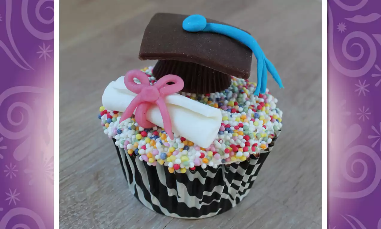 Cupcake met zwart-wit gestreept bakje, kleurrijke suikerparels, chocolade baret, fondant diploma met roze strik en blauwe versiering