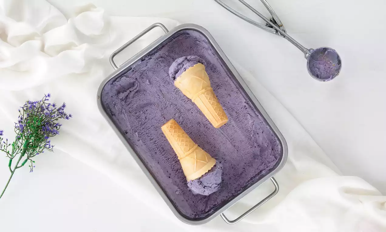 Mor renkli pürüzsüz yaban mersinli dondurma, metal tepside sunulmuş, üzerine yerleştirilmiş iki külah ve yanına konmuş dondurma kaşığıyla