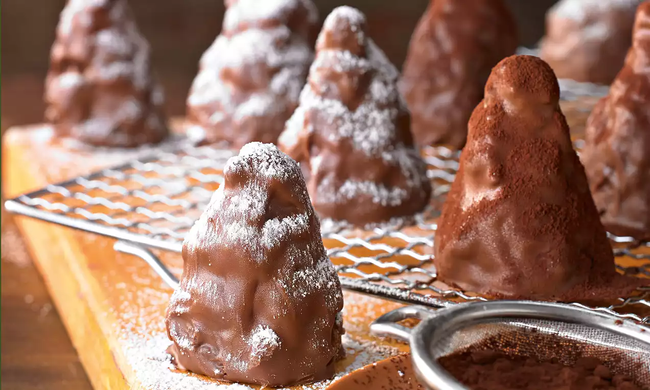 Schoko-Berge schokoladige Türmchen mit Keksbröseln und hellen Keksstücken, glänzender Schokoladenglasur und Puderzucker auf weißem Teller