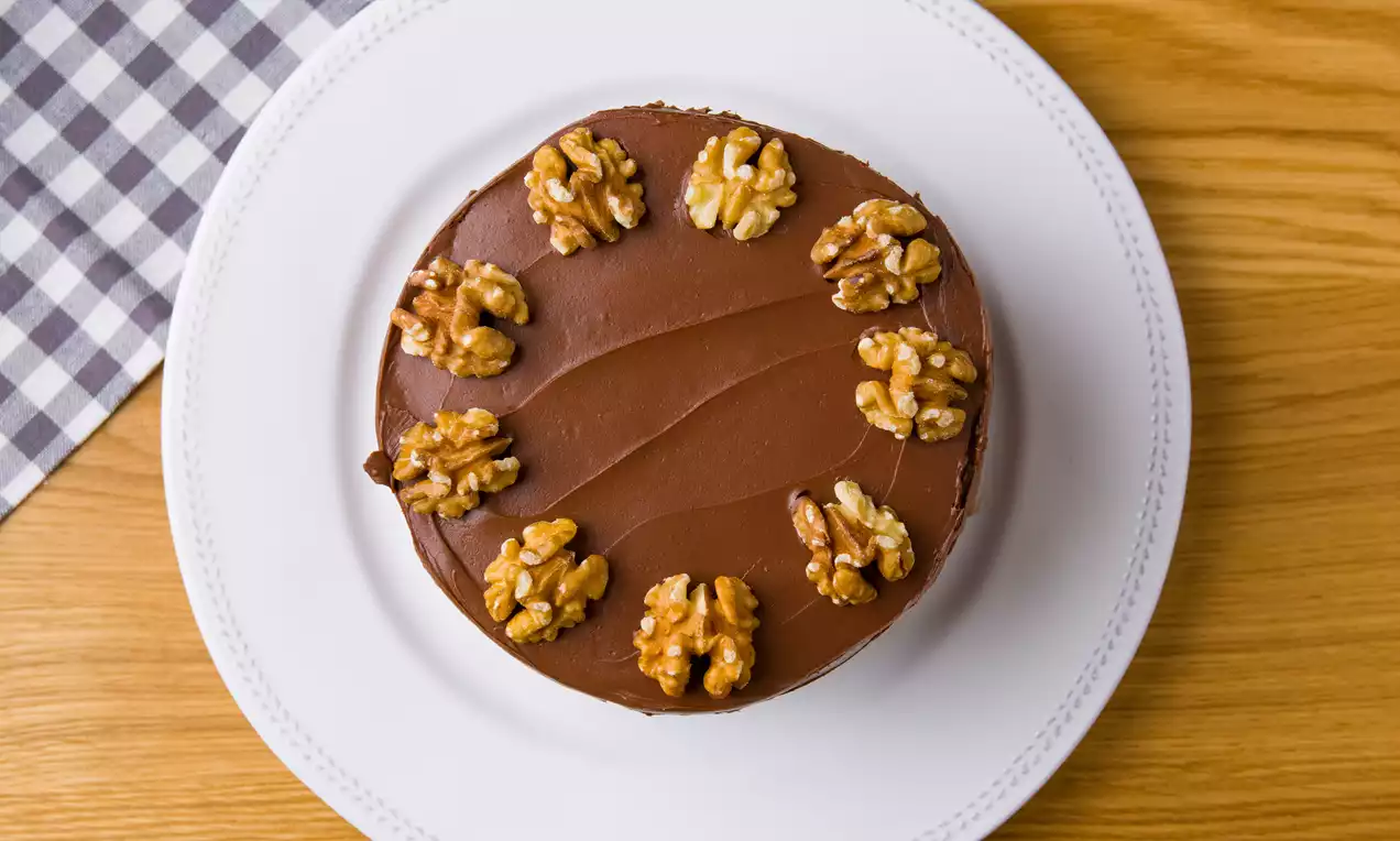 Tarta circular de chocolate brillante decorada con nueces doradas distribuidas simétricamente sobre un plato blanco