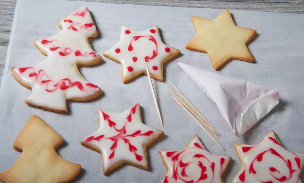 Açık renkli hamurdan yapılmış yılbaşı yıldızı ve çam ağacı şekilli kurabiyeler, beyaz ve kırmızı şekerlemelerle desenlenmiş.