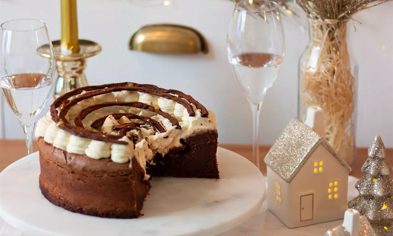 Плътна кръгла шоколадова торта с кремообразна спирала от бял крем и тъмен шоколад, сервирана на бяла стойка сред празнична декорация