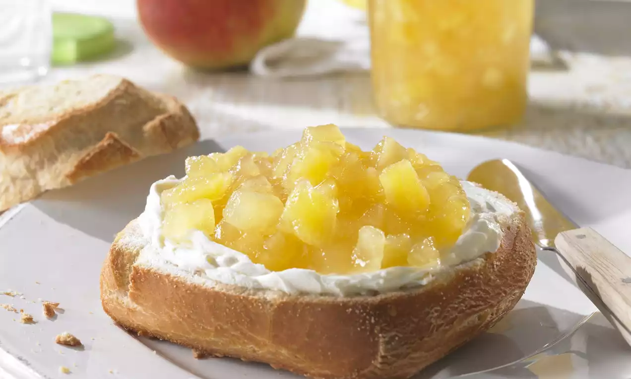 Povestează despre dulceață galben-aurie de mere și ananas cu bucăți translucide, întinsă peste frișcă pe o felie de pâine prăjită