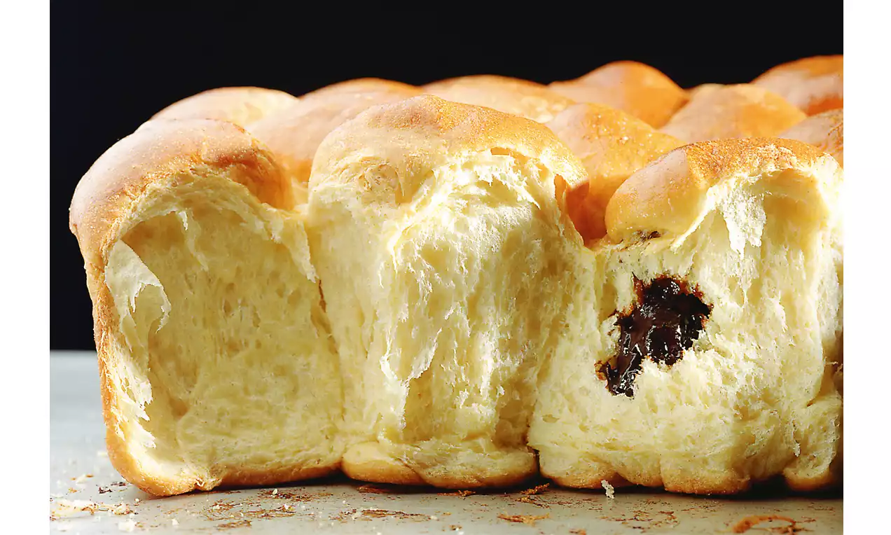 Licht goudbruine buchteln met zachte, luchtige structuur, gedeeltelijk gescheurd om donkere vulling van zoete jam te onthullen