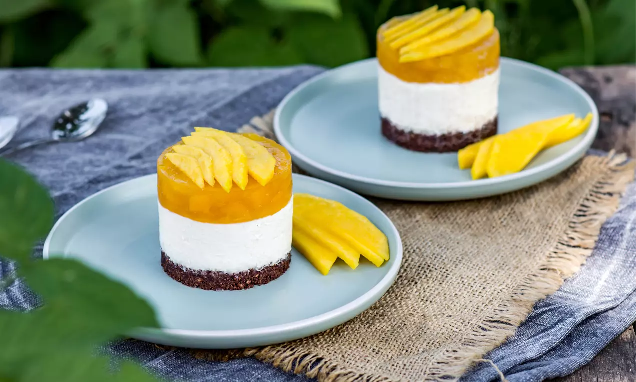 Кръгли мини десерти с ярко жълта манго глазура и подредени резени манго върху кремообразна бяла основа и кафяво бисквитено дъно