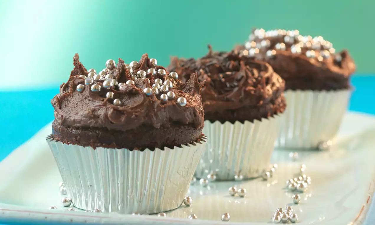 Chokolade-cupcakes med luftig, mørkebrun topping toppet med sølvfarvede sukkerperler i sølvforme på et lyst fad