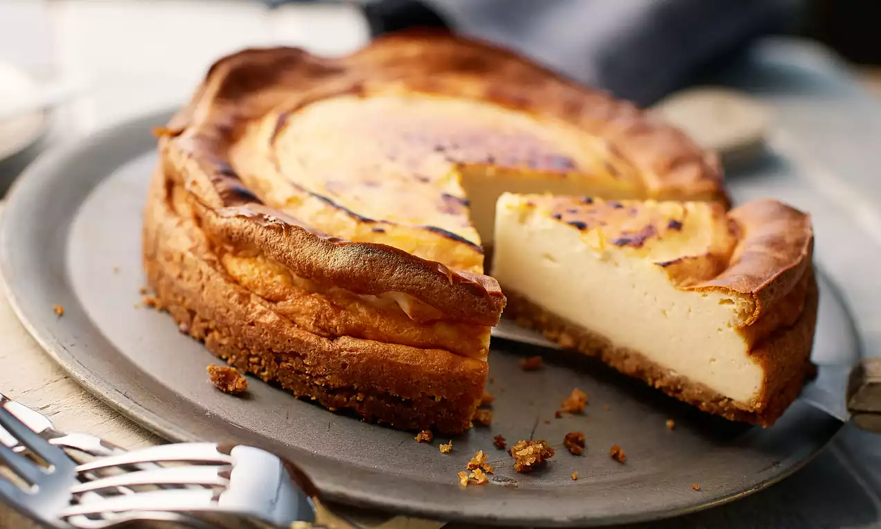 Goldbrauner Cheesecake mit karamellisierter Oberfläche und cremiger Füllung auf knusprigem Keksboden, angerichtet auf einem grauen Teller