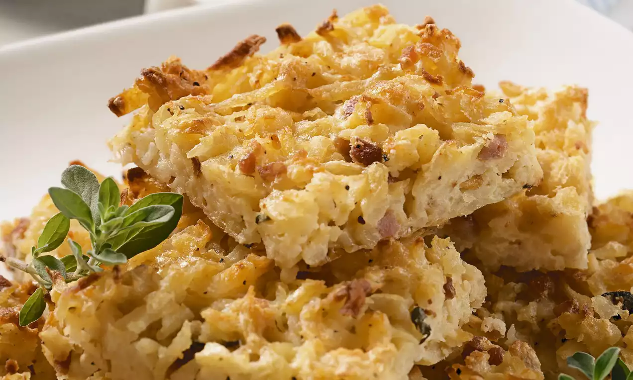 Goldbraune Rösti-Ecken mit knuspriger Oberfläche und feiner Kartoffeltextur, leicht geschichtet auf weißem Teller mit frischem Kräuterzweig