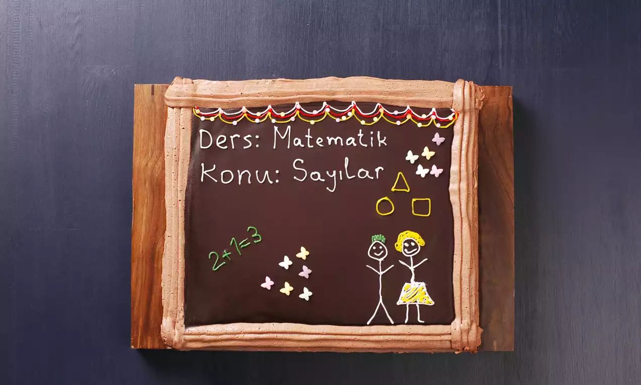 Tahta görünümünde siyah çikolata kaplı pasta, renkli süslemelerle çevrili, üstü el çizimi figürler ve geometrik şekillerle dekore edilmiş