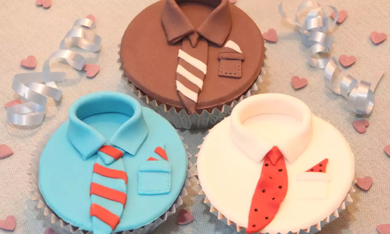 Cupcakes met fondant in bruine, blauwe en witte stropdasvorm, gestyled met strepen, stippen en kleine decoratieve hartjes op beige doek