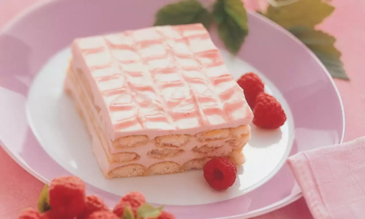 Tiramisu aux framboises rectangulaire avec couches de biscuits imbibés et crème rose pâle sur une assiette mauve, entouré de framboises fraîches