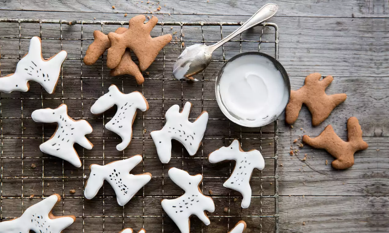 Biscuits en forme de rennes bruns glacés de blanc, sur une grille métallique avec un bol de glaçage et une cuillère argentée