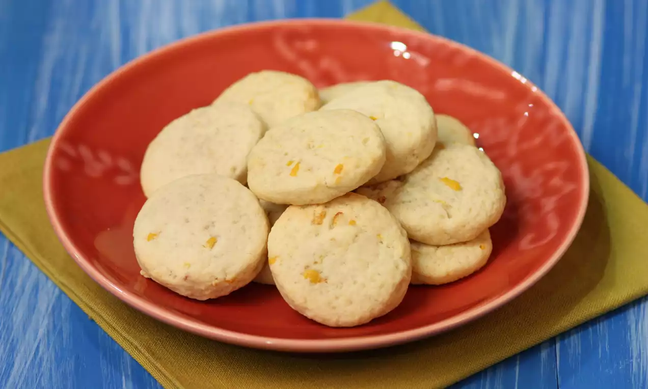 Yuvarlak ve hafif kabarık limonlu kurabiyeler, pürüzsüz dokulu, sarı detaylar içeren kırmızı tabakta, zeytin yeşili örtü üzerinde