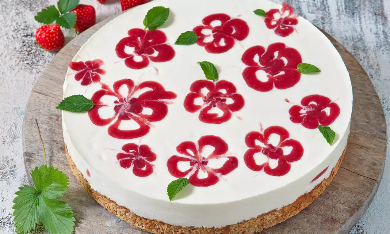 Ořechový dort s bílým krémem zdobený červenými jahodovými květy a zelenými lístky na světlé hnědé křehké krustě na dřevěném podkladu