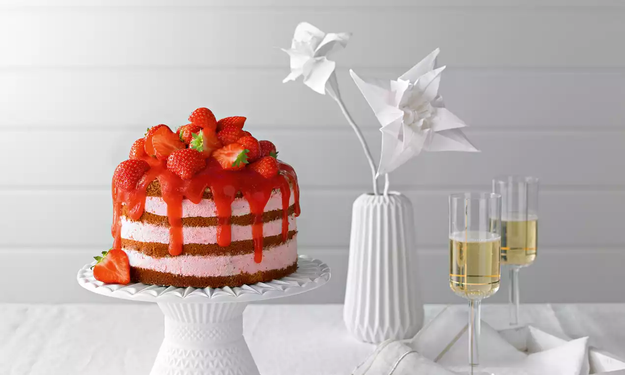 Rote Erdbeeren und glänzende Glasur als frischer Akzent auf einer geschichteten Torte mit rosa Creme auf weißer Tortenplatte drapiert