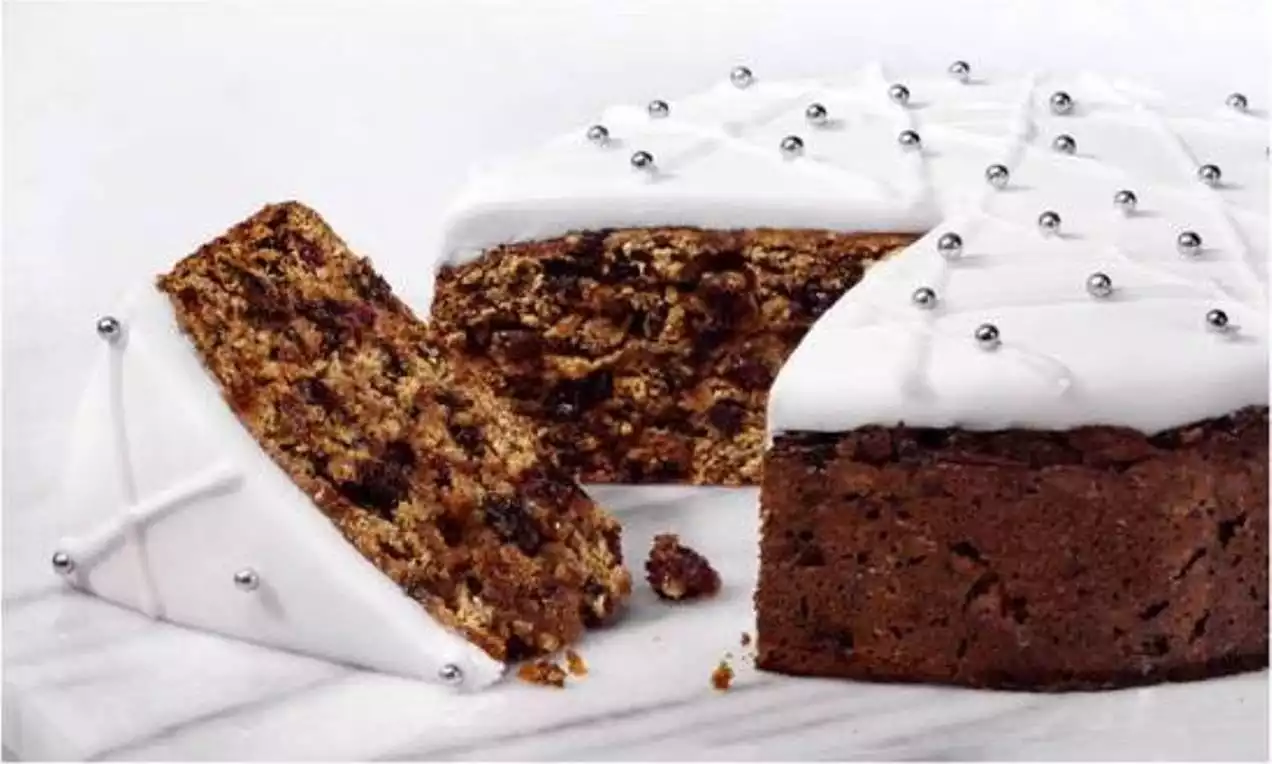 Christmas fruitcake with dense, dark brown crumb speckled with dried fruit, topped with smooth white icing and silver ball decorations