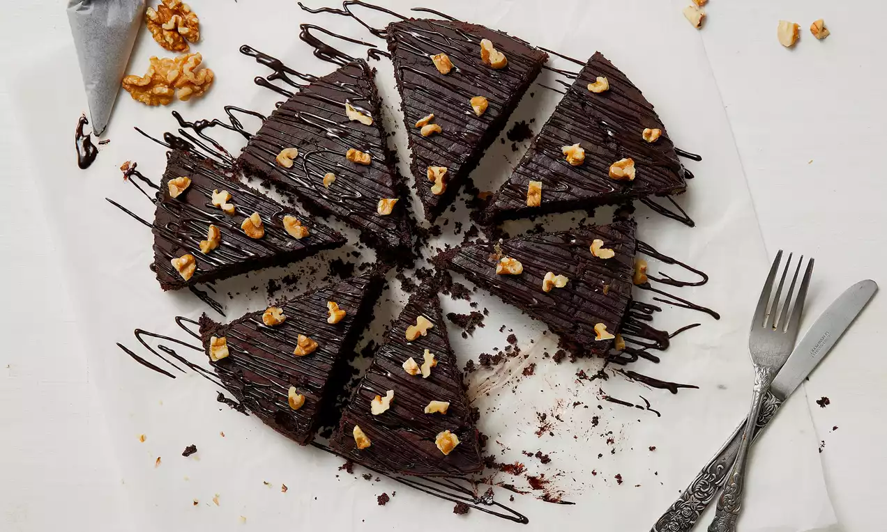 Koyu renkli yoğun çikolatalı vegan kek dilimleri, üstünde ceviz parçaları ve çikolata sosu ile beyaz zeminde düzenlenmiş şık sunum