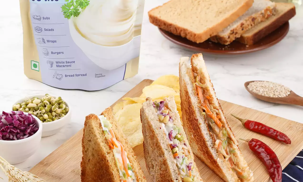Triangular brown bread sandwiches filled with creamy coleslaw in shades of white, orange, and purple, arranged on a wooden board