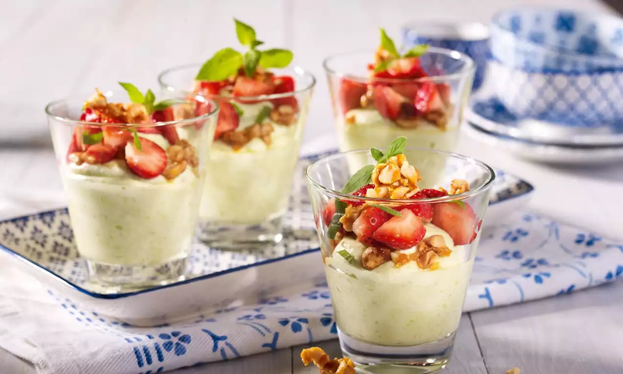 Zartgrüne Avocado-Zitronen-Mousse in Gläsern, getoppt mit glänzenden roten Erdbeerstückchen, Walnüssen und frischen Minzblättern auf blau-weißem Geschirr