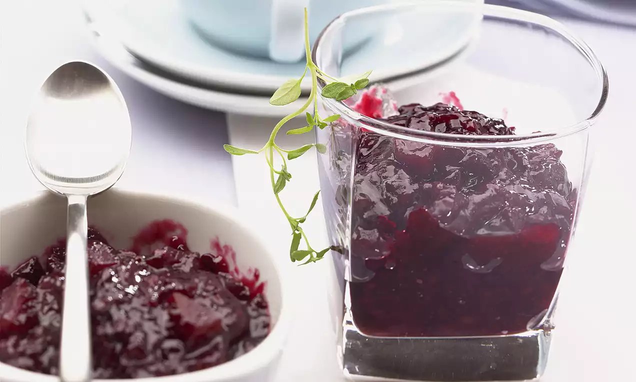 Confettura di more e pere viola intenso, lucida e cremosa, servita in bicchiere trasparente con rametto decorativo e ciotola accanto