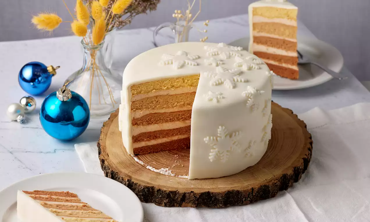 Weiße Ombre-Torte mit sanften Farbschichten von Creme bis Karamell, dekoriert mit Schneeflocken auf einem Holzbrett serviert