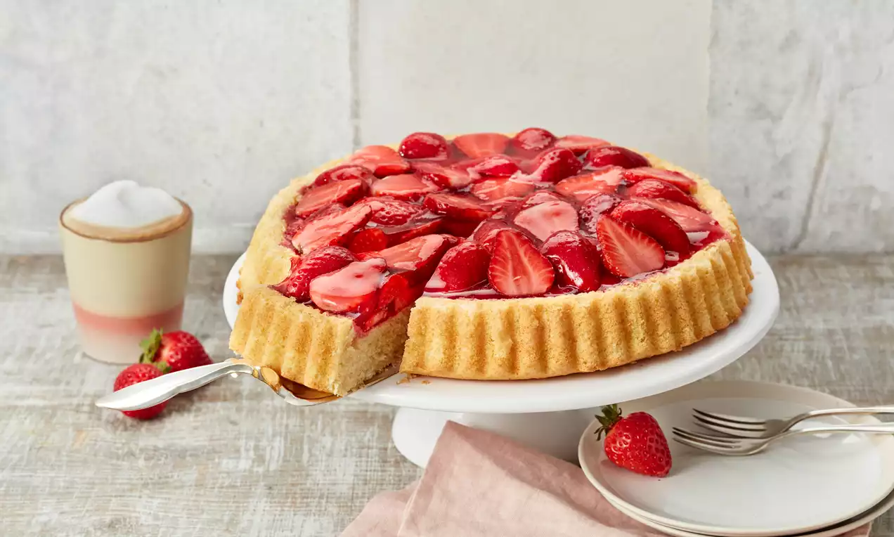 Erdbeerkuchen mit glänzenden roten Erdbeeren, hellem Biskuitboden und zartem Tortenguss, dekoriert mit Minzblatt