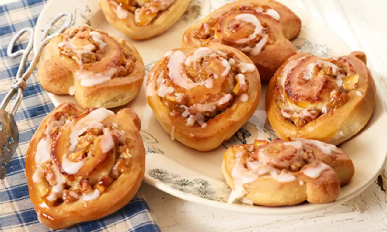 Petites brioches dorées en spirales garnies de cannelle, morceaux de pomme et glaçage blanc, disposées sur une assiette en céramique