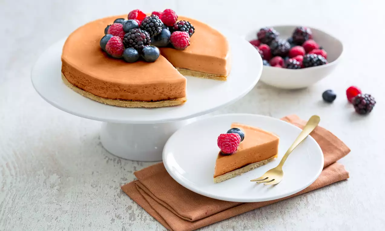 Chocolade cheesecake met gladde, bruine bovenlaag op een lichte koekbodem, gegarneerd met rood en donker bosfruit op een witte taartstandaard