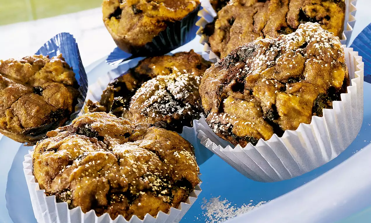 Muffins dorés et moelleux parsemés de myrtilles, aux formes irrégulières, présentés dans des caissettes blanches et saupoudrés de sucre
