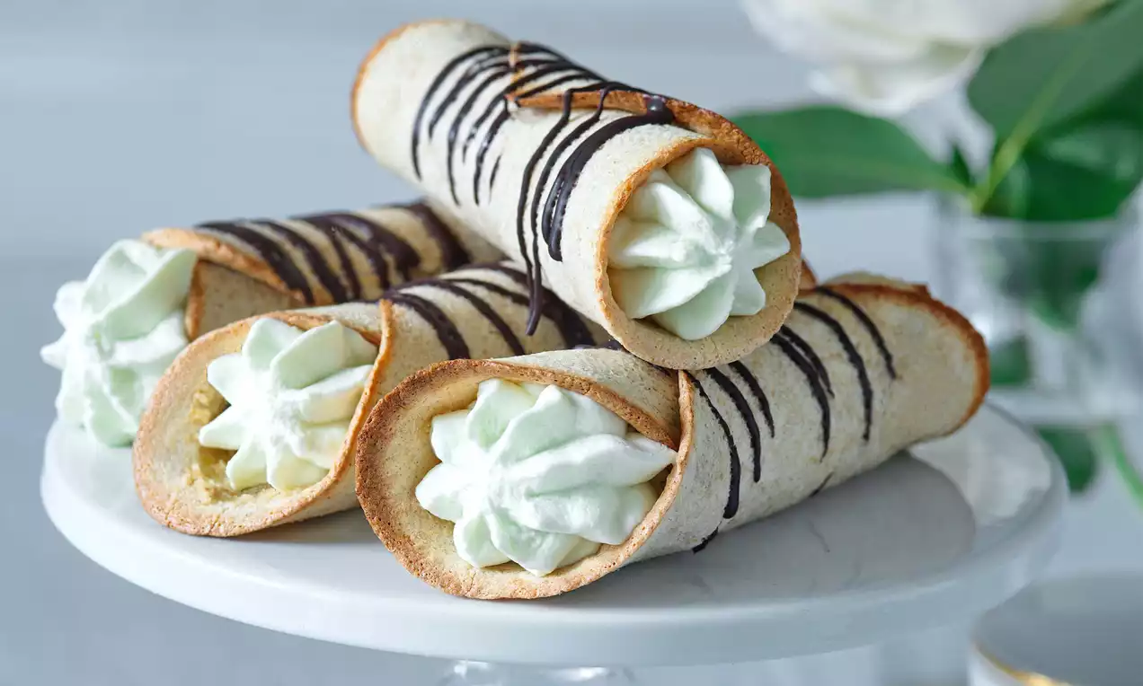 Griliášové trubičky světle hnědé barvy se svislými proužky čokolády, plněné krémově bílou pěnou, uspořádané na bílém stojanu