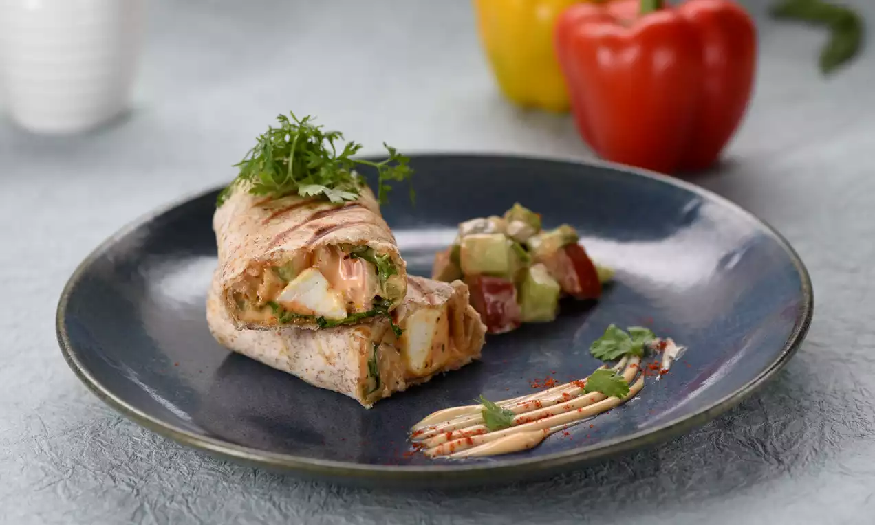 Achari paneer wrap with golden crisp edges, filled with pale paneer cubes and vegetables, garnished with fresh herbs on a dark plate