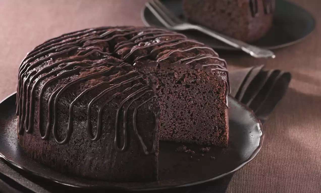 Rich, dark chocolate cake with a moist texture, drizzled with glossy chocolate glaze, served on a matte black plate