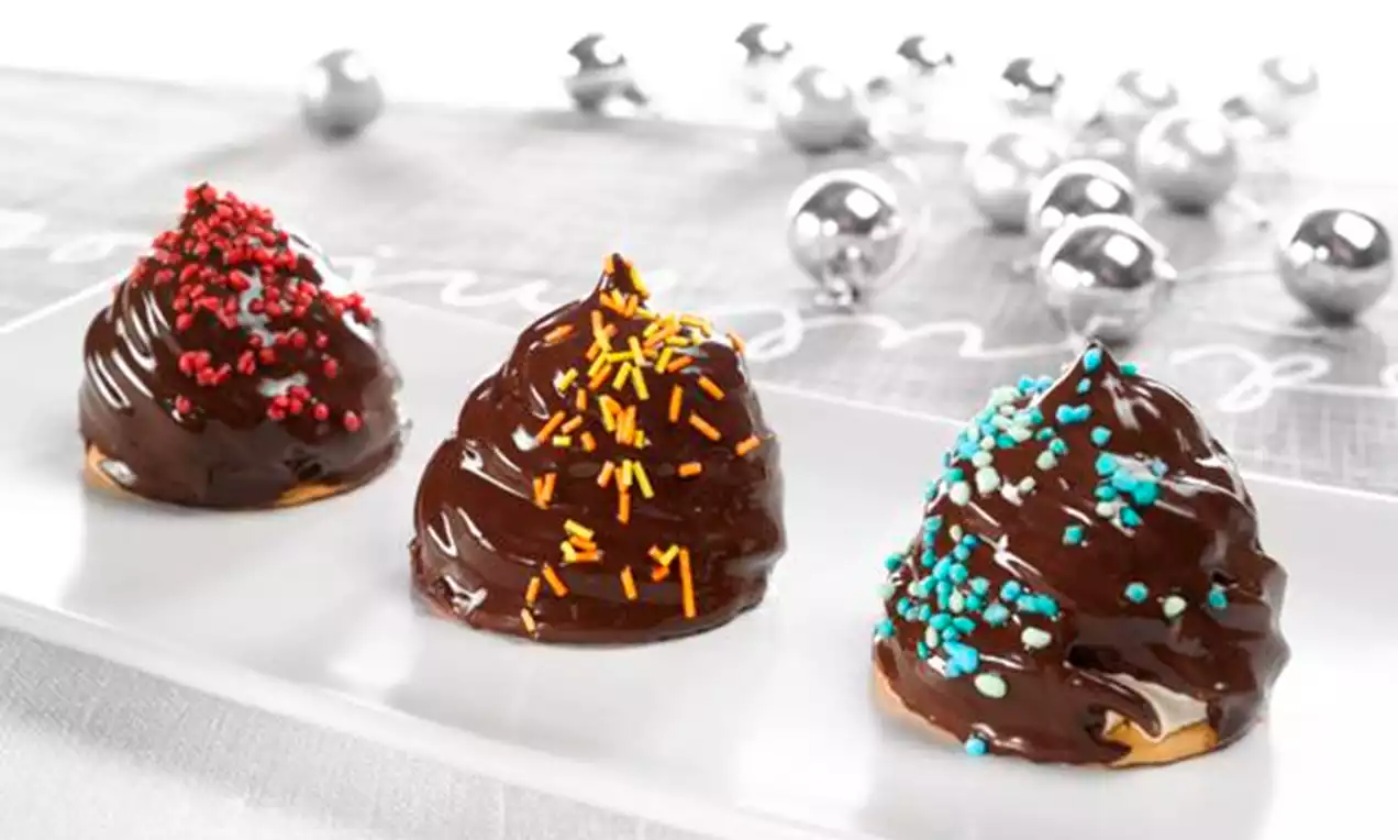 Kolme kiiltävää suklaakuorrutteista vaahtokarkkipupua valkoisella suorakaiteen muotoisella lautasella, koristeltu värikkäillä rakeilla.