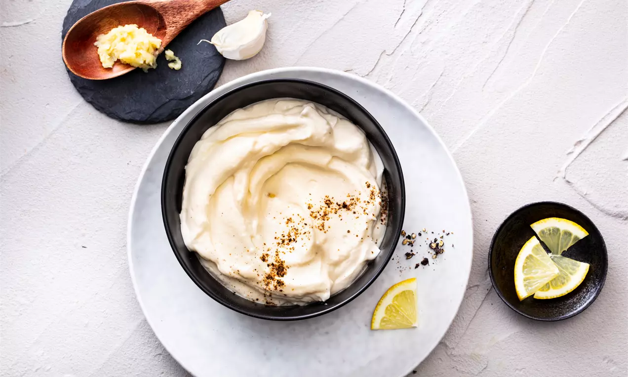 Гладък и пухкав крем със светъл жълтеникав оттенък, поръсен с подправки, в черна купа върху сива чиния с резени лимон