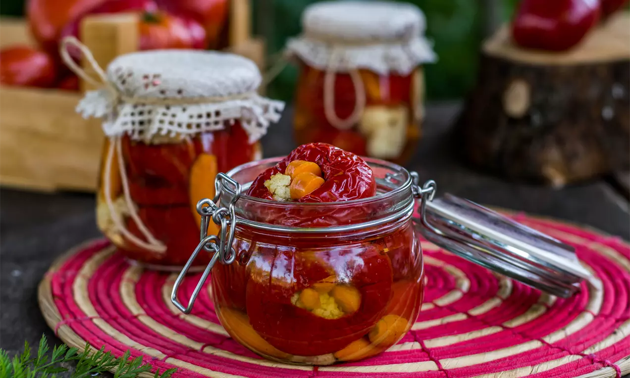 Червени печени камби с лъскава текстура, внимателно подредени в стъклен буркан с метална закопчалка върху пъстра текстилна подложка