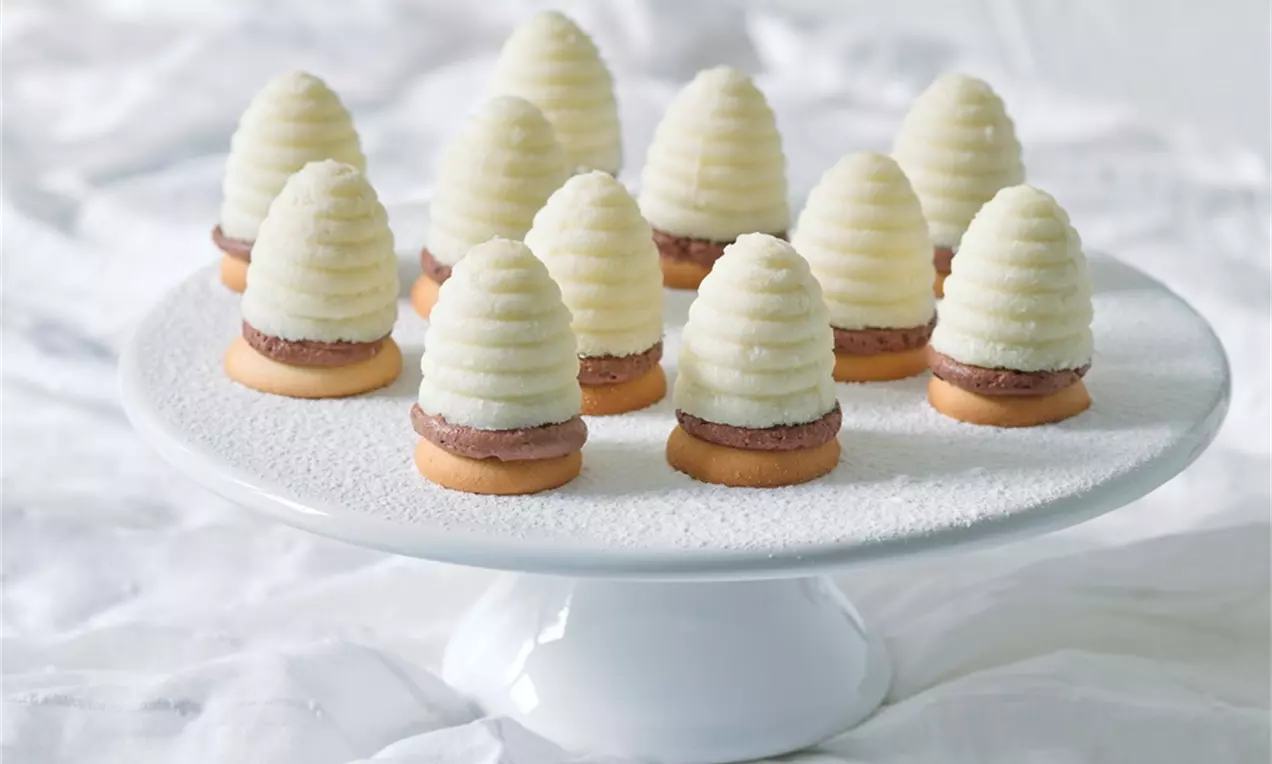 Krémově bílé vosí hnízda ve tvaru žebrovaného kužele usazené na kulatých sušenkách, na bílém podnosu z porcelánu s jemným reliéfem